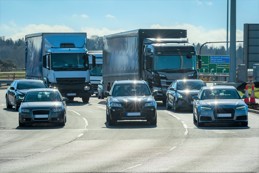 Multiple trucks and cars merging on a motorway in bright daylight with strong sun glare reflecting off windscreens
