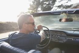 Man wearing sunglasses driving a classic convertible on a sunny day, viewed from the passenger seat