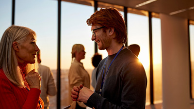 A man and a woman speaking to each other in a crowded room lit by the sun