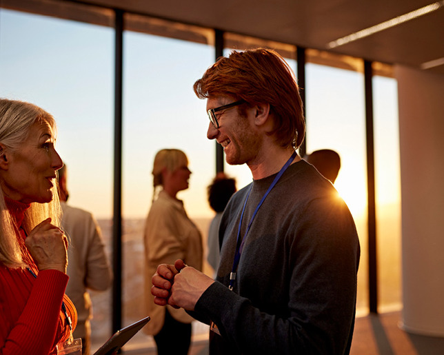 A man and a woman speaking to each other in a crowded room lit by the sun